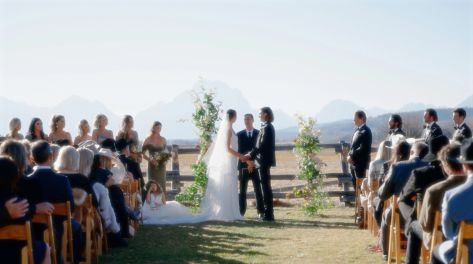 wedding taking place in a field with the Tetons in the background. and wedding happening infront o fwood fence