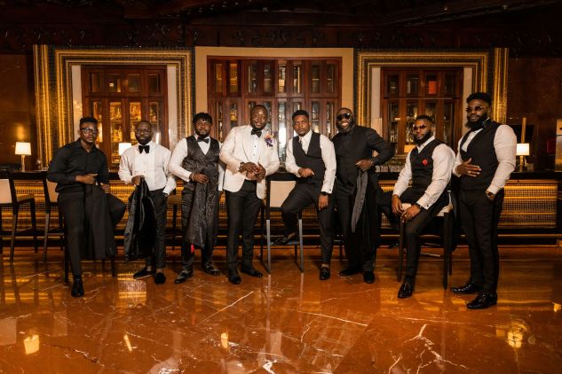 groomsmen in a row with groom in the middle. in dark toned room with wood bar behind them