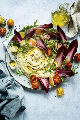 Hummus with red envide and half cherry tomatoes spread around and olive oil drizzled on the top