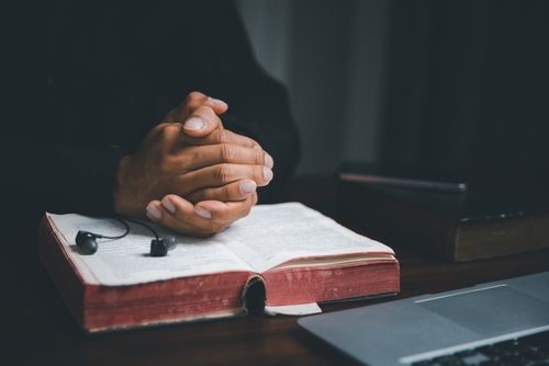 Someone resting their hands on a holy book in front of a computer.