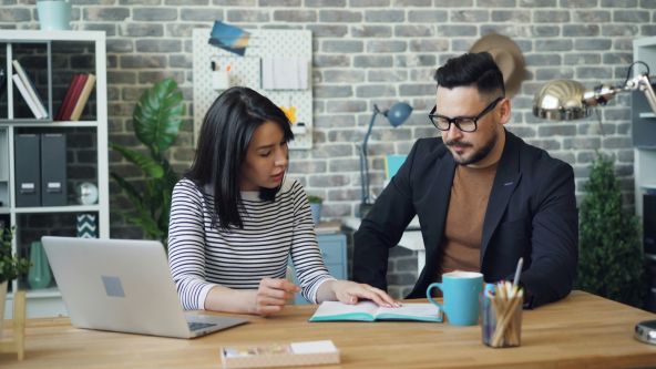 A couple sitting at a desk working on a financial planner and they have a computer open